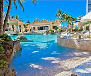 A resort pool area with clear blue water, palm trees, and lounge chairs. - The Towers Chevron Renaissance Holidays Gold Coast (Surfers Paradise)