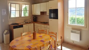 A kitchen with wooden cabinets, a stove, and a dining table with chairs. - Quiet holiday home in Les Vans with pool (Les Vans)