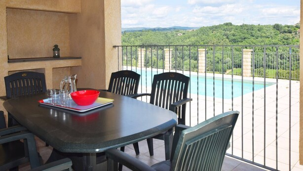 A dining area with a table and chairs, overlooking a swimming pool and a scenic view of a green landscape. - Quiet holiday home in Les Vans with pool (Les Vans)