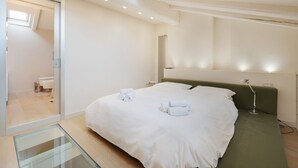 Quarto de hotel moderno com uma cama grande, piso de vidro para a varanda e vista para o banheiro.