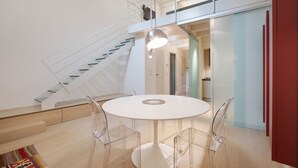 Um interior moderno com uma mesa branca arredondada, cadeiras transparentes, uma escada e um armário vermelho.