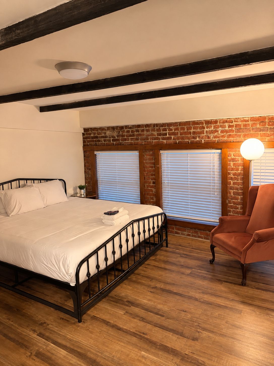 A bedroom with a bed, a chair, and a brick wall.