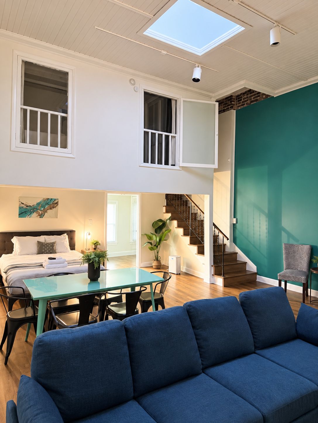 Un amplio salón con un sofá, una mesa de comedor y una escalera que lleva a un nivel superior.
