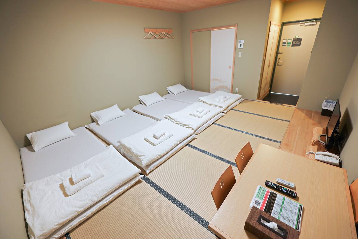 A hotel room with four single beds, a wooden table with a remote control, a tissue box, and a small chair.