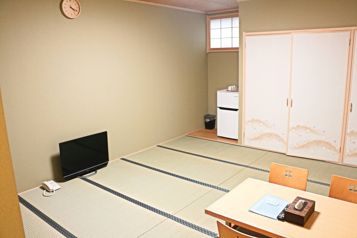 A room with tatami flooring, a television, a desk with a chair, and a wardrobe.