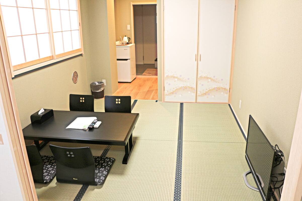 A room with tatami mats, a tatami mat table, black chairs, a black desk, and a computer.