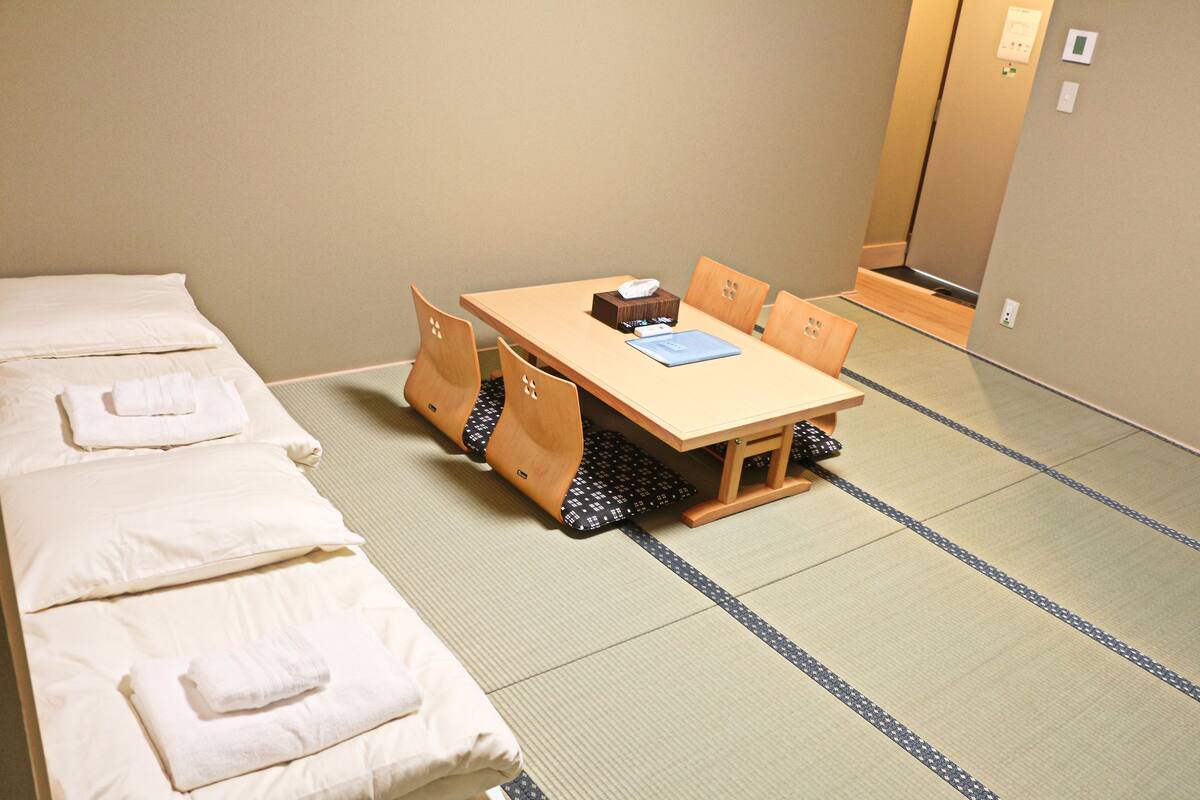 A room with a bed, a table with chairs, and a tatami mat floor.