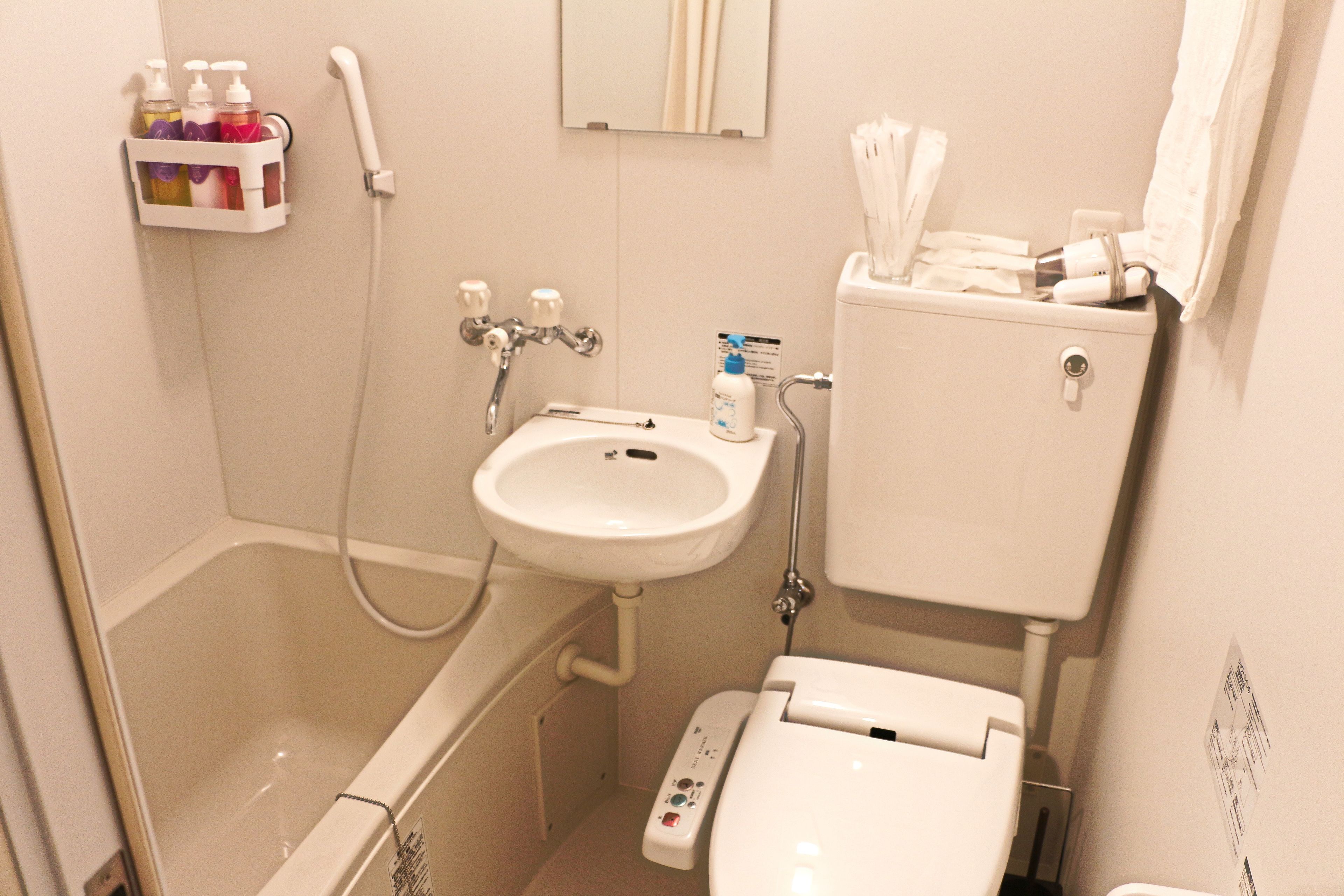 Un bany amb banyera, un lavabo i un vàter. Hi ha una prestatgeria amb articles de tocador i un penjador de tovalloles.