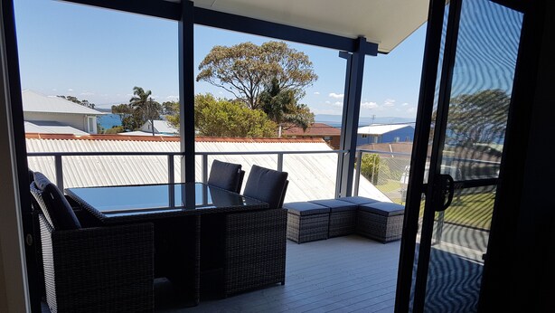 A balcony with wicker furniture and a glass door leading outside. - "LAZY DAYZ" Currarong beach home.   50m from unspoilt beaches and walking tracks (Currarong)