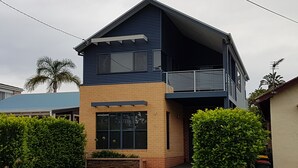A two-story house with a balcony, brick foundation, and a blue roof. - "LAZY DAYZ" Currarong beach home.   50m from unspoilt beaches and walking tracks (Currarong)
