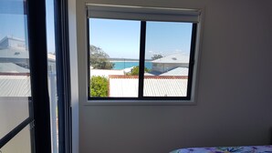 A room with a large window offering a view of buildings and a body of water. - "LAZY DAYZ" Currarong beach home.   50m from unspoilt beaches and walking tracks (Currarong)