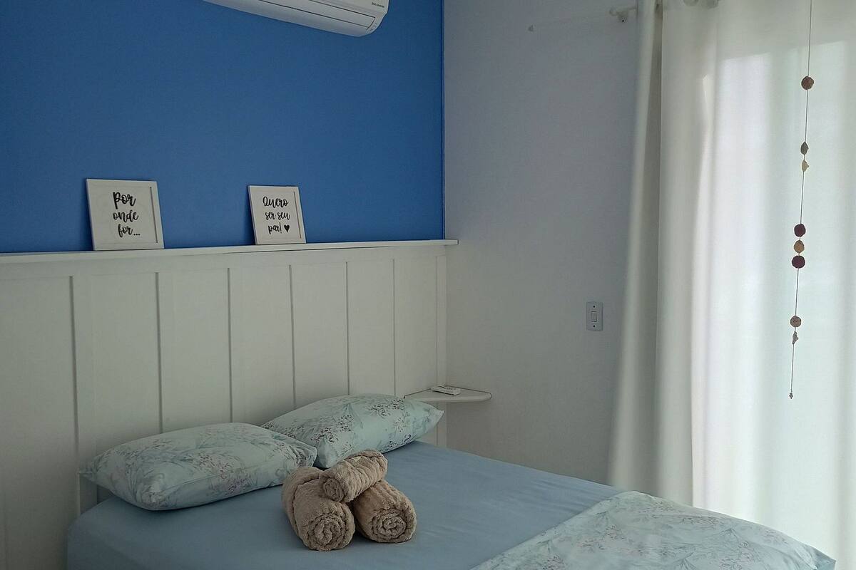 Une chambre à coucher avec un lit, des oreillers, une table de chevet et un climatiseur fixé au mur.