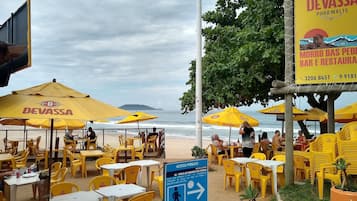Mobiliário de exterior com guarda-sóis amarelos e mesas, vista para a praia e um aviso a indicar acesso público.