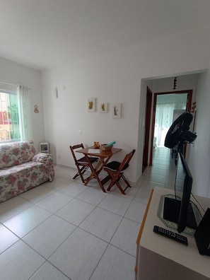A living room with a sofa, a dining table with chairs, a TV, and artwork on the wall.