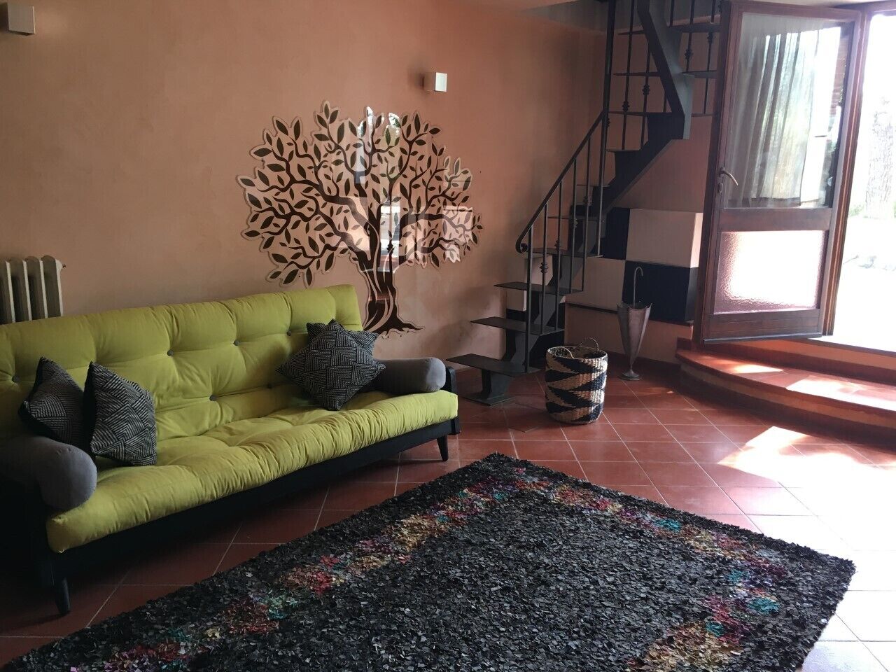 A living room with a green sofa, a colorful rug, a wall art piece, and a staircase.