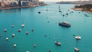 Ein Yachthafen mit zahlreichen dort vertäuten Booten, eine Stadtansicht im Hintergrund und freie Sicht auf das Wasser.