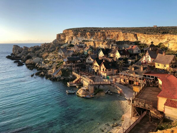A coastal village with traditional houses, a wooden pier, and a rocky cliff.