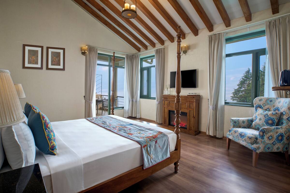 A bedroom with a large bed, a chair, a television, and a fireplace.