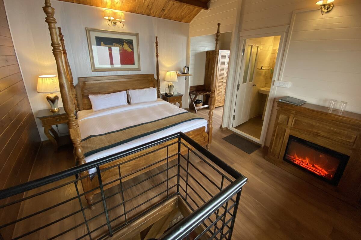 A bedroom with a four-poster bed, a fireplace, a wooden ceiling, and a painting on the wall.