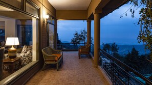 A balcony with wicker chairs, a table with a lamp, and a view of mountains. - Larisa Resort, Mussoorie (Dehradun)