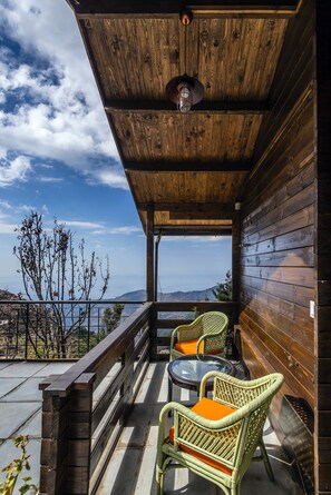A wooden balcony with wicker chairs and a table, overlooking a mountainous landscape. - Larisa Resort, Mussoorie (Dehradun)
