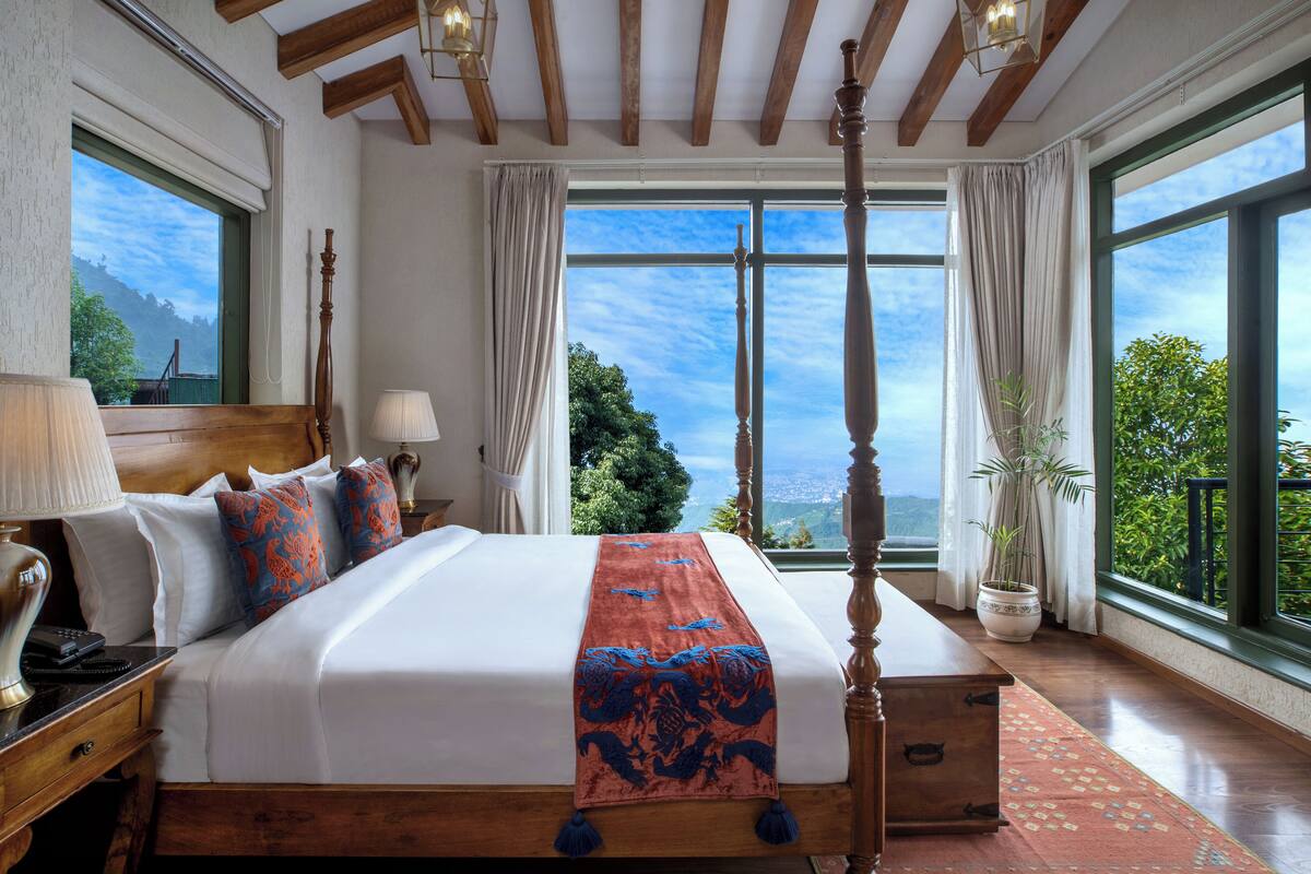 A spacious bedroom with a large bed, a wooden headboard, and a view of the outdoors through large windows.