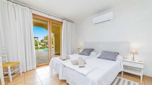 Ein Hotelzimmer mit einem großen Bett, zwei Nachttischen, einem Sessel und Blick auf Pool und Grünflächen.