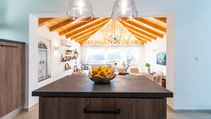 Een ruime keuken met een groot eiland, houten balken in het plafond, hanglampen, en een schaal met citroenen op het eiland.
