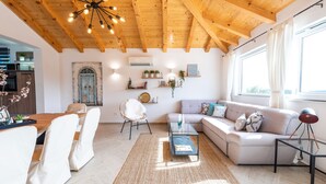 Een moderne woonkamer met een houten plafond, een bank, een glazen salontafel en een eethoek met stoelen en een tafel.