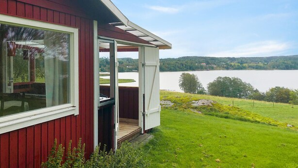 Een rood gebouw met een overdekte veranda met uitzicht op een meer en een gazon.