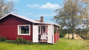 Een klein, laag vakantiehuisje, rood met een witte veranda en een schoorsteen.