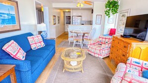 A living room with a blue sofa, wicker coffee table, and patterned armchairs. - Experience Tilghman Beach and Racquet Club Unit 208! Oceanfront, Pools, Tennis, Close to Main Street! (North Myrtle Beach)