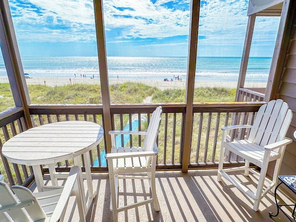 A covered outdoor area with a view of the beach, featuring a table and two chairs.