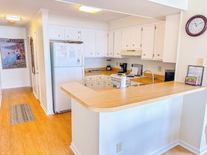 A kitchen with white cabinets, a wooden countertop, a refrigerator, a stove, and a clock on the wall.