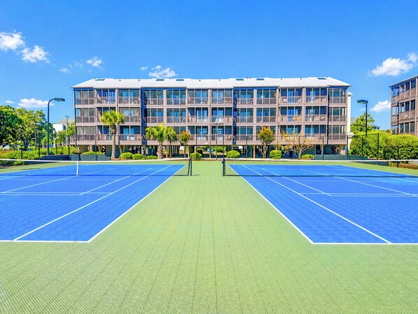 A tennis court with a net, surrounded by a building with multiple balconies and windows.