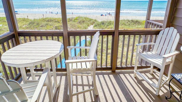 A wooden deck with a table and chairs, overlooking a beach with people in the distance. - Experience Tilghman Beach and Racquet Club Unit 208! Oceanfront, Pools, Tennis, Close to Main Street! (North Myrtle Beach)