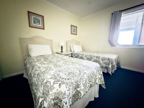 A hotel room with two beds, a small table, and a window with blinds. - Tilghman Beach and Racquet Club 304 (North Myrtle Beach)