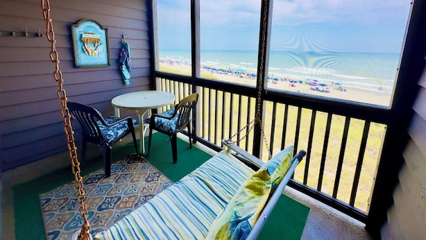 A room with a view of the beach, a swing, a table with chairs, and a framed picture on the wall. - Experience Tilghman Beach and Racquet Club Unit 304! Oceanfront, Pools, Tennis, Close to Main Street! (North Myrtle Beach)