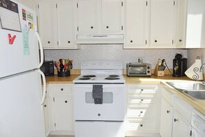 A kitchen with white cabinets, a stove, a microwave, a toaster, and a sink.