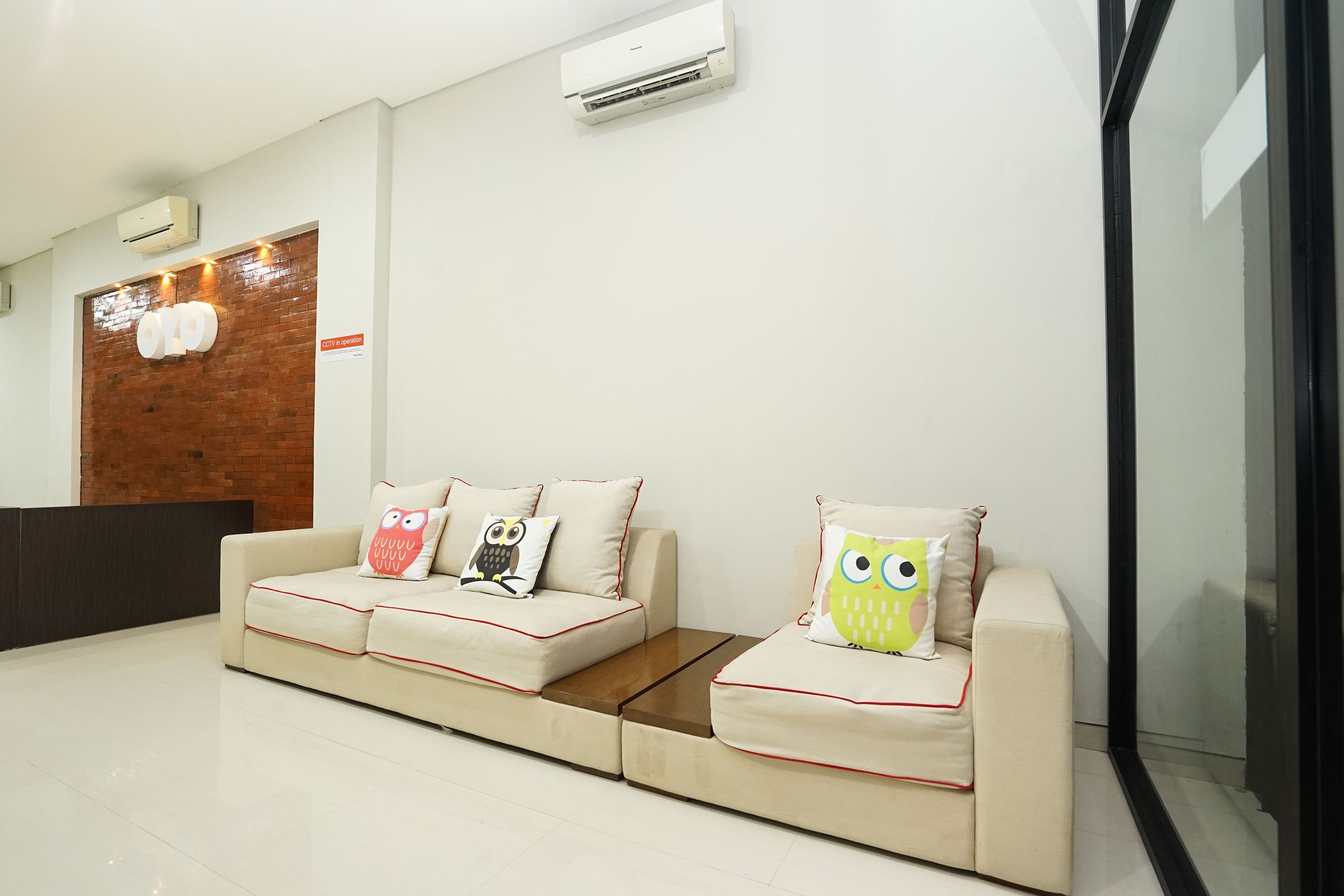 A reception area with a beige sofa, two owl-themed pillows, and an air conditioning unit on the wall.