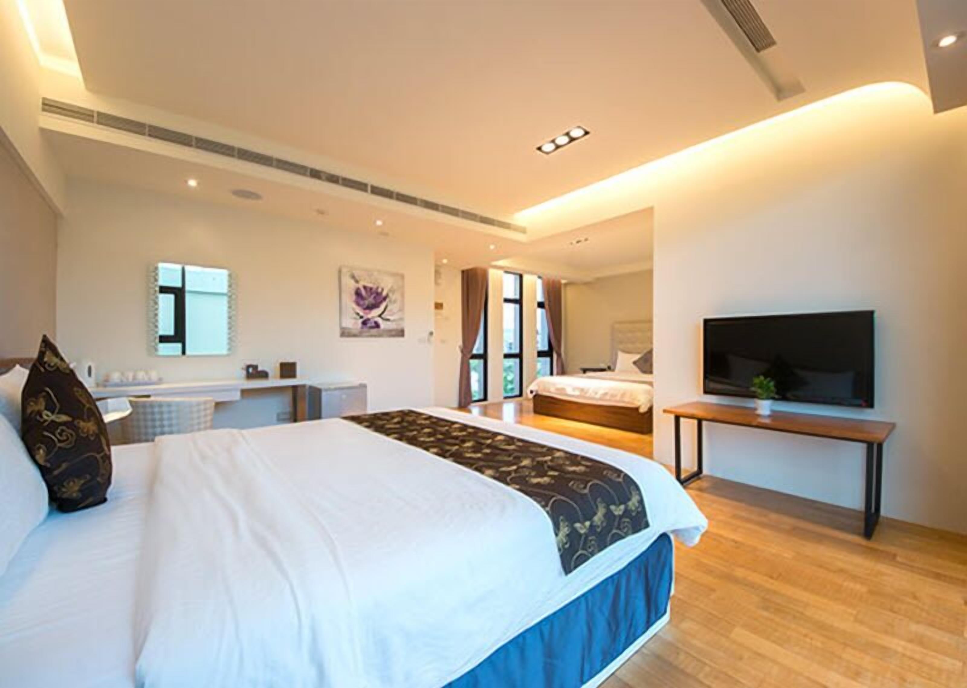 A modern hotel room with a large bed, a TV, a desk, and a bathroom visible through an open door.