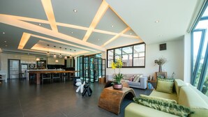 Een ruime woonkamer met een groot raam, een keuken op de achtergrond en een modern plafondontwerp.
