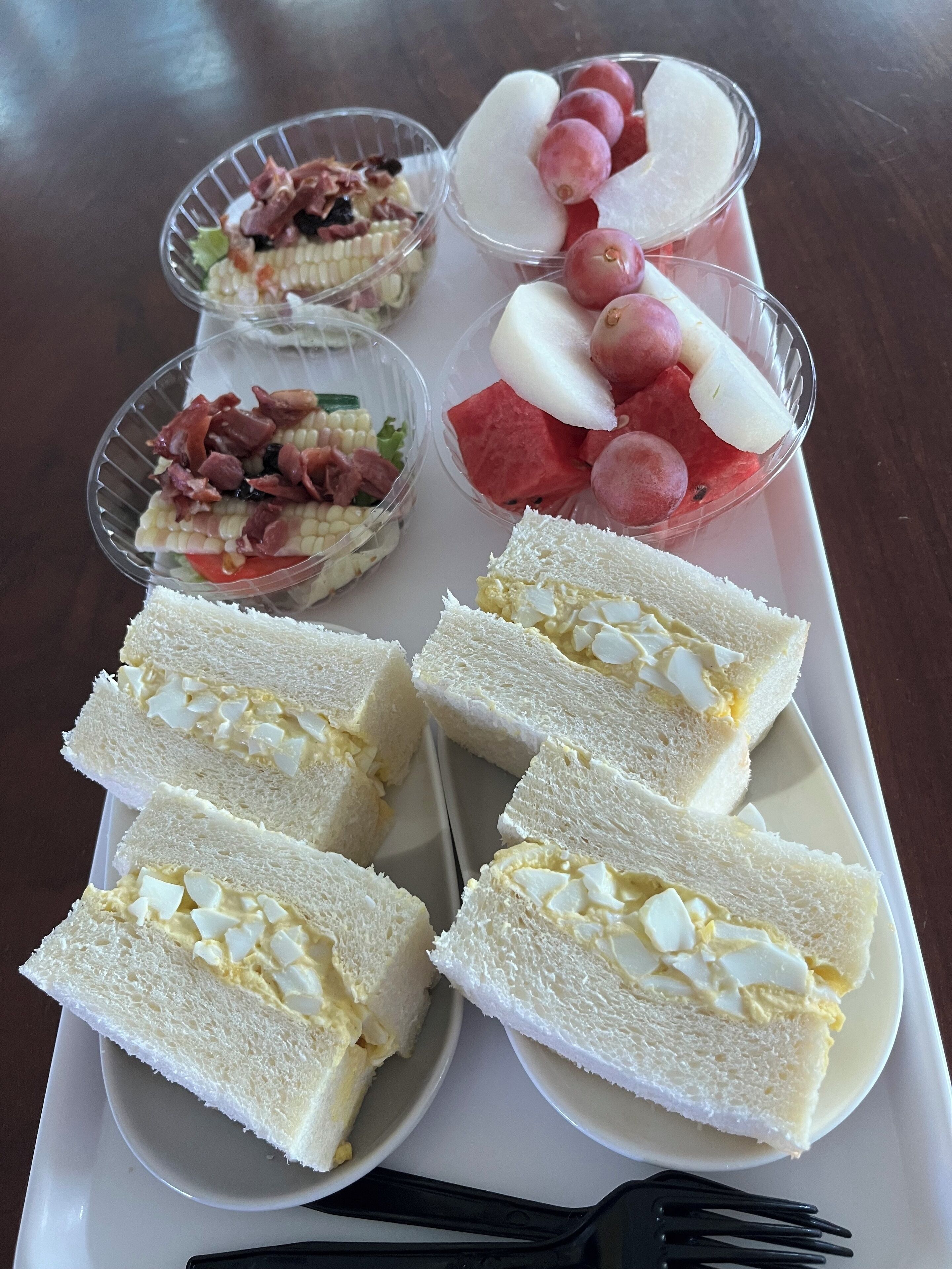 A tray with various food items including sandwiches, fruit, and a salad.
