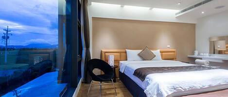 Una habitación de hotel moderna con un ventanal grande, una cama, una mesita de noche y una silla.