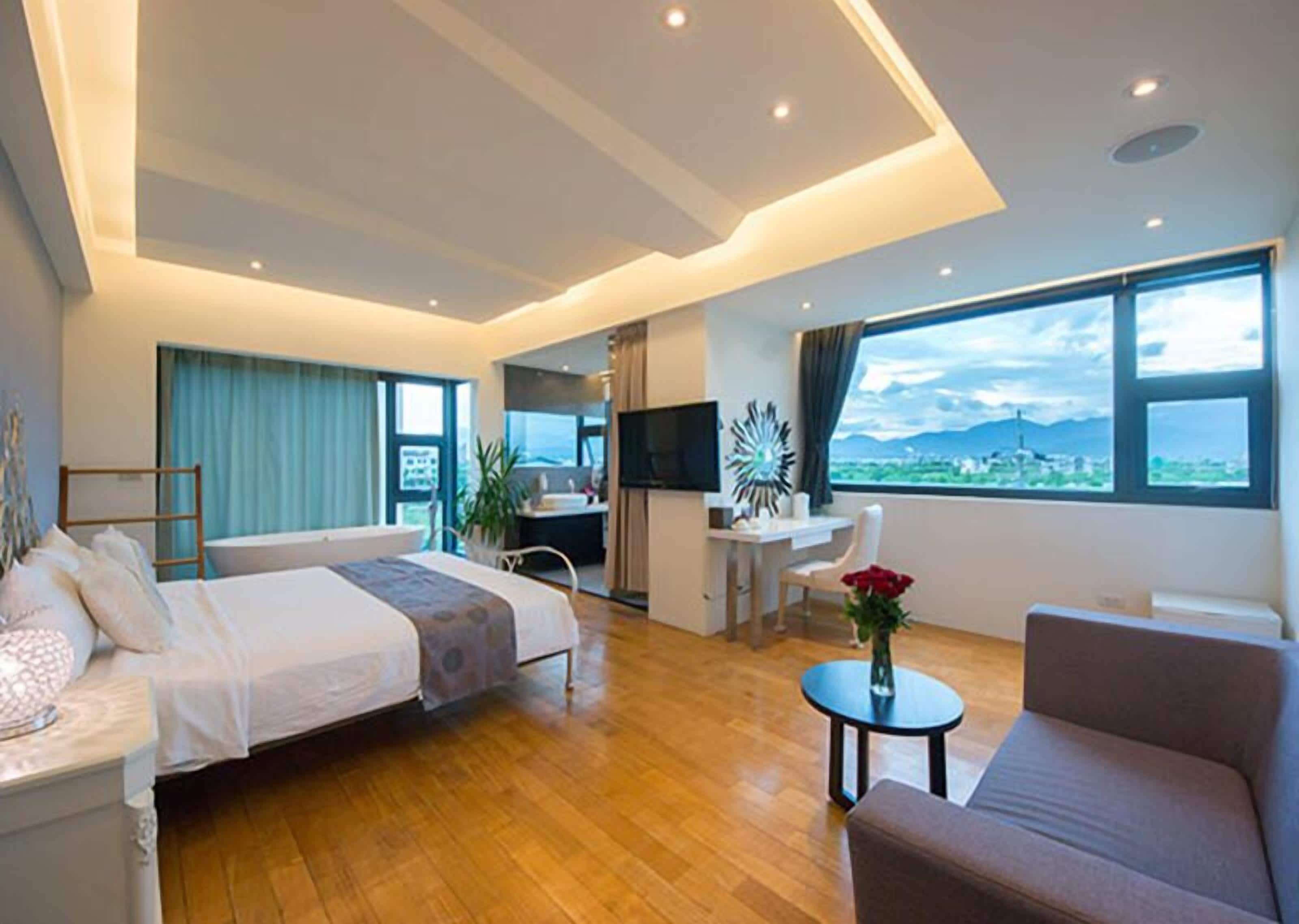 Una habitación de hotel moderna con una cama grande, un escritorio, un sofá y vistas a la ciudad.