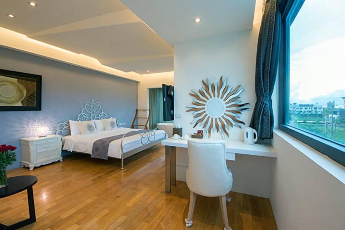 Un dormitorio moderno con cama, escritorio y silla, un ventanal con vistas, y un adorno en la pared con forma de sol.