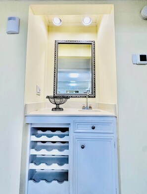 Un baño con espejo, lavamanos y espacio para guardar vino.