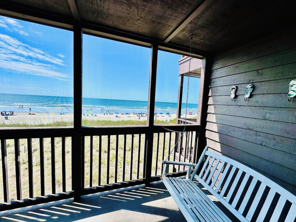 Une vue sur la plage depuis un porche abrité, avec un banc.