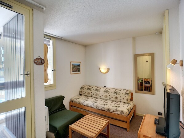 A small, cozy room with a sofa, a chair, a small table, a TV, and a mirror.