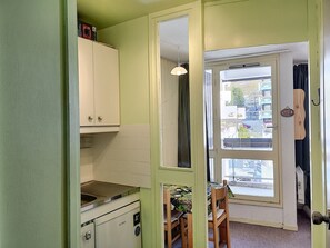 A compact kitchen with white cabinets, a sink, and a stove. There is a dining area with a table and chairs.